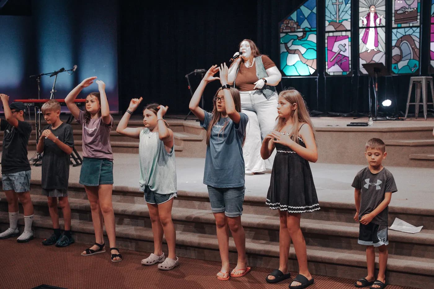 Kids doing worship motions with a leader on stage