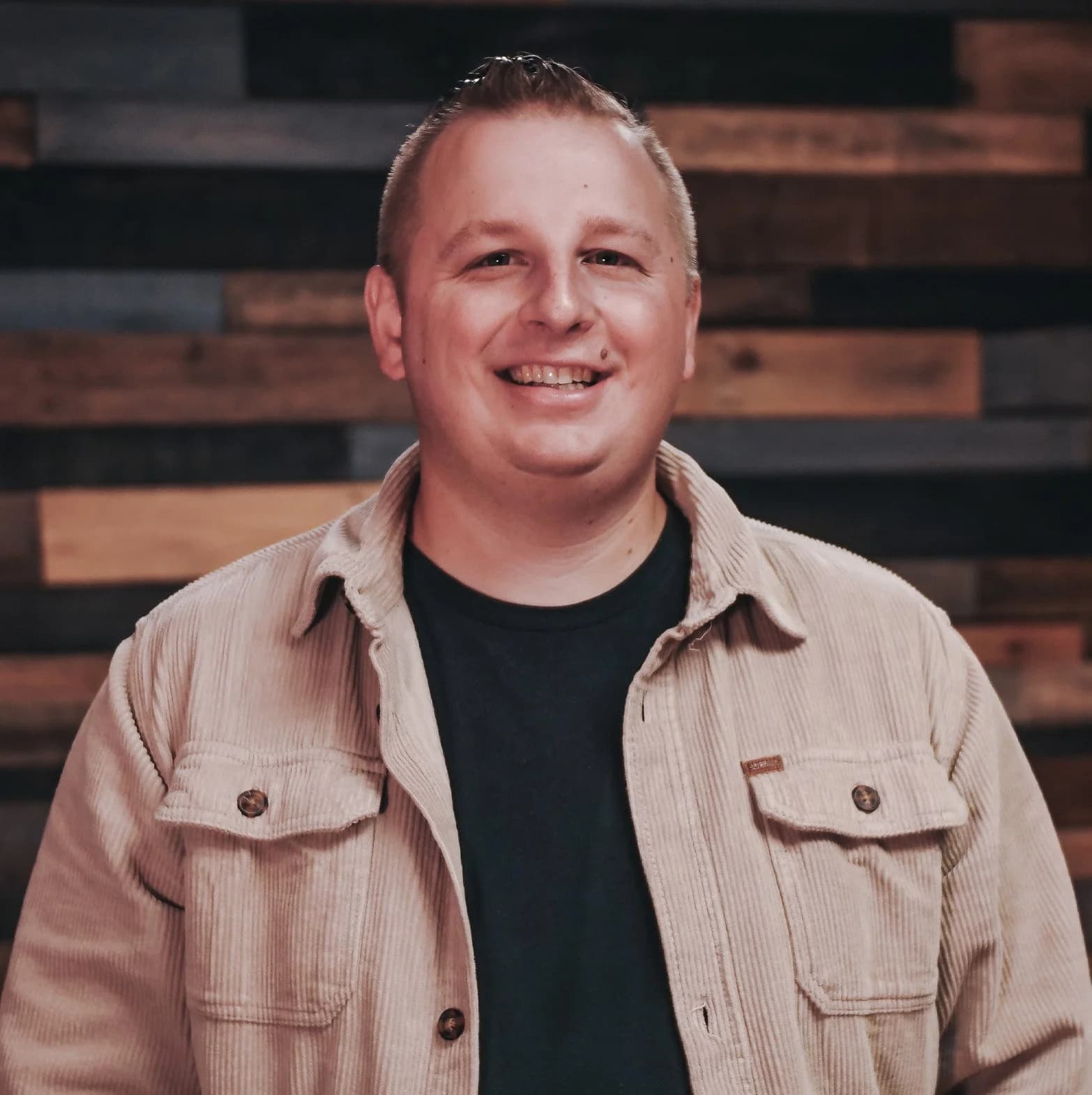Bryan Thiel-Aquilina smiling in front of a wooden wall